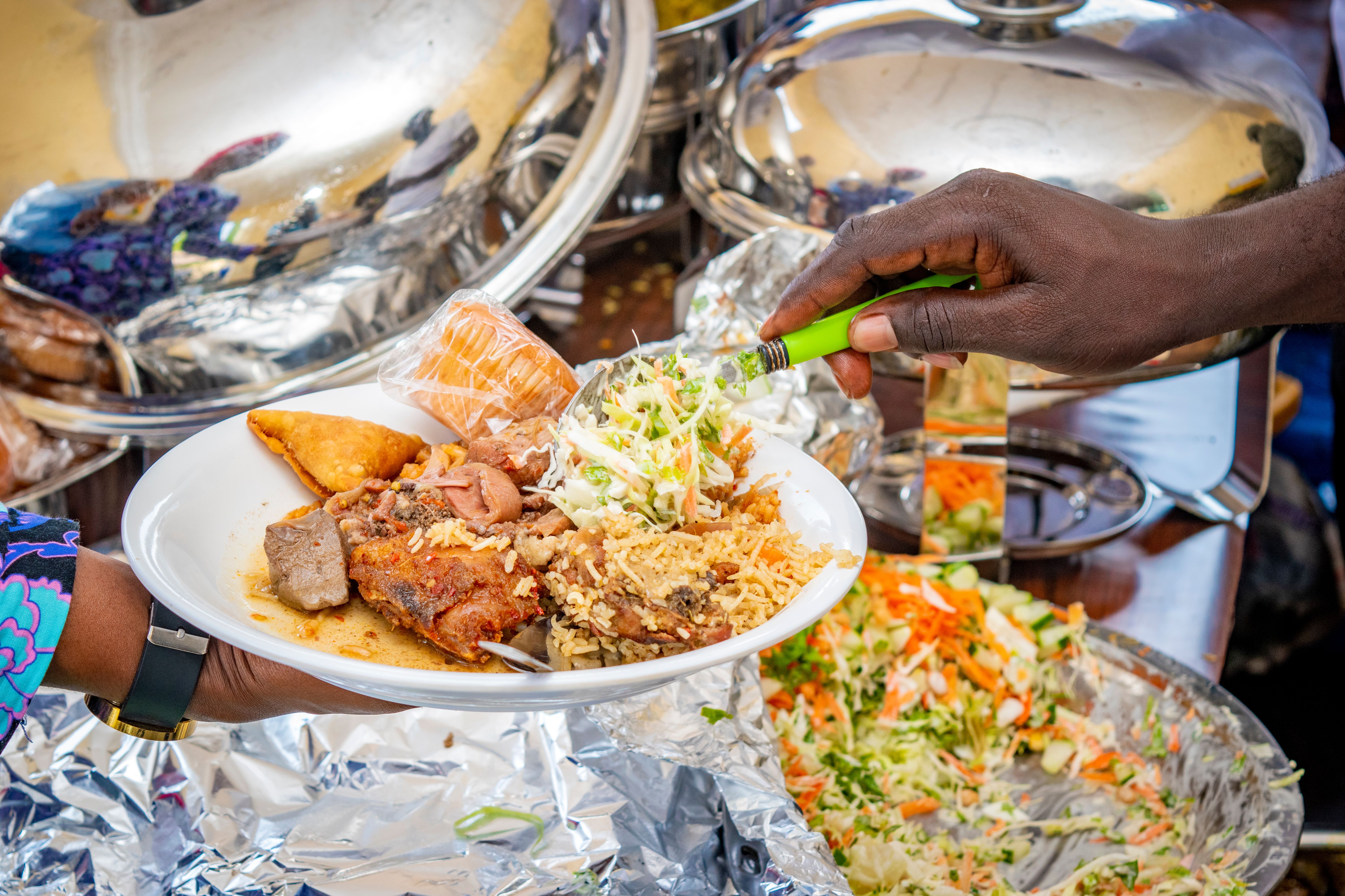 A cook shop lunch plate of chicken, rice, coleslaw and a fried pastry being served from steam trays