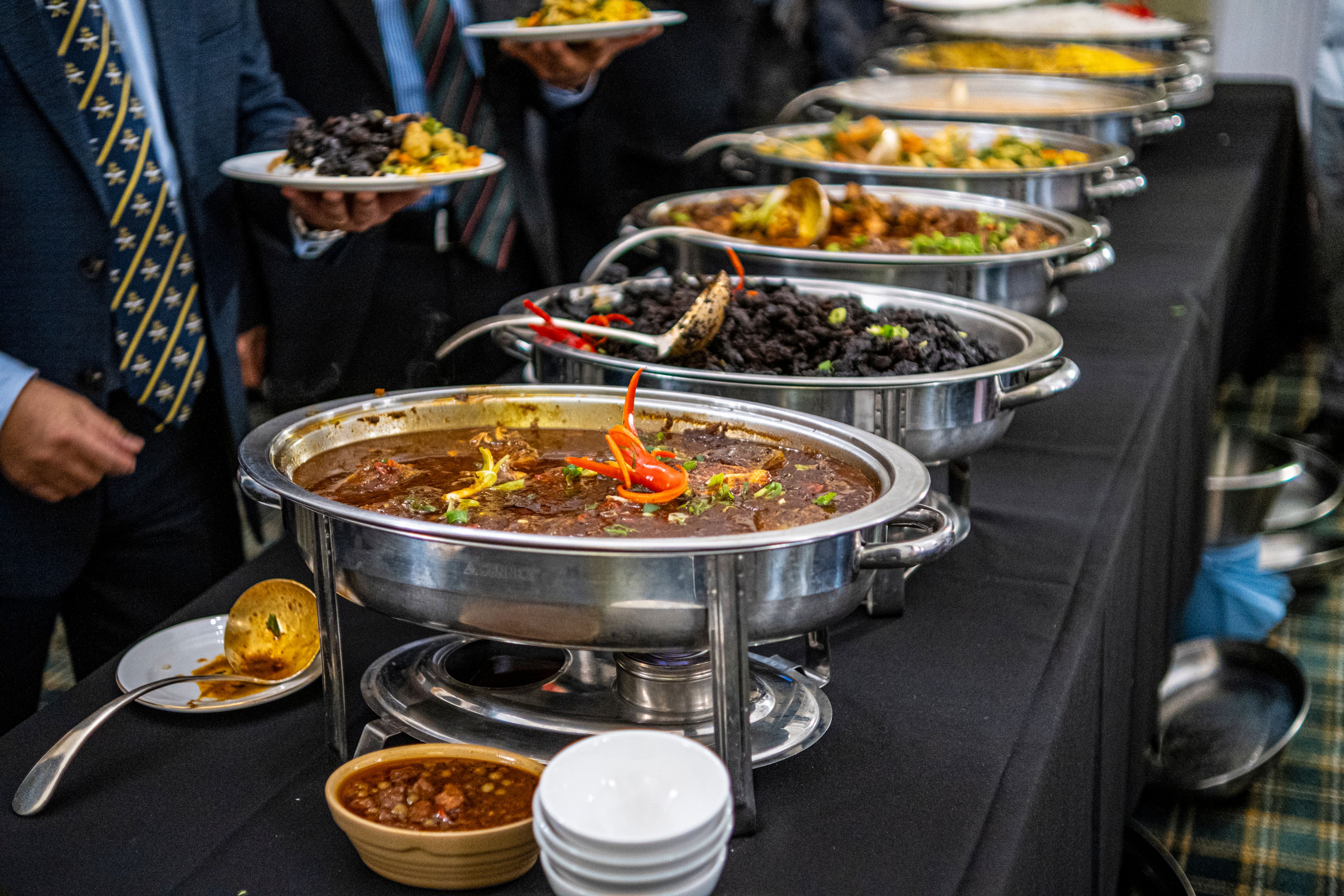 A row of chafing dishes at a Guyanese wedding buffet with guests serving themselves