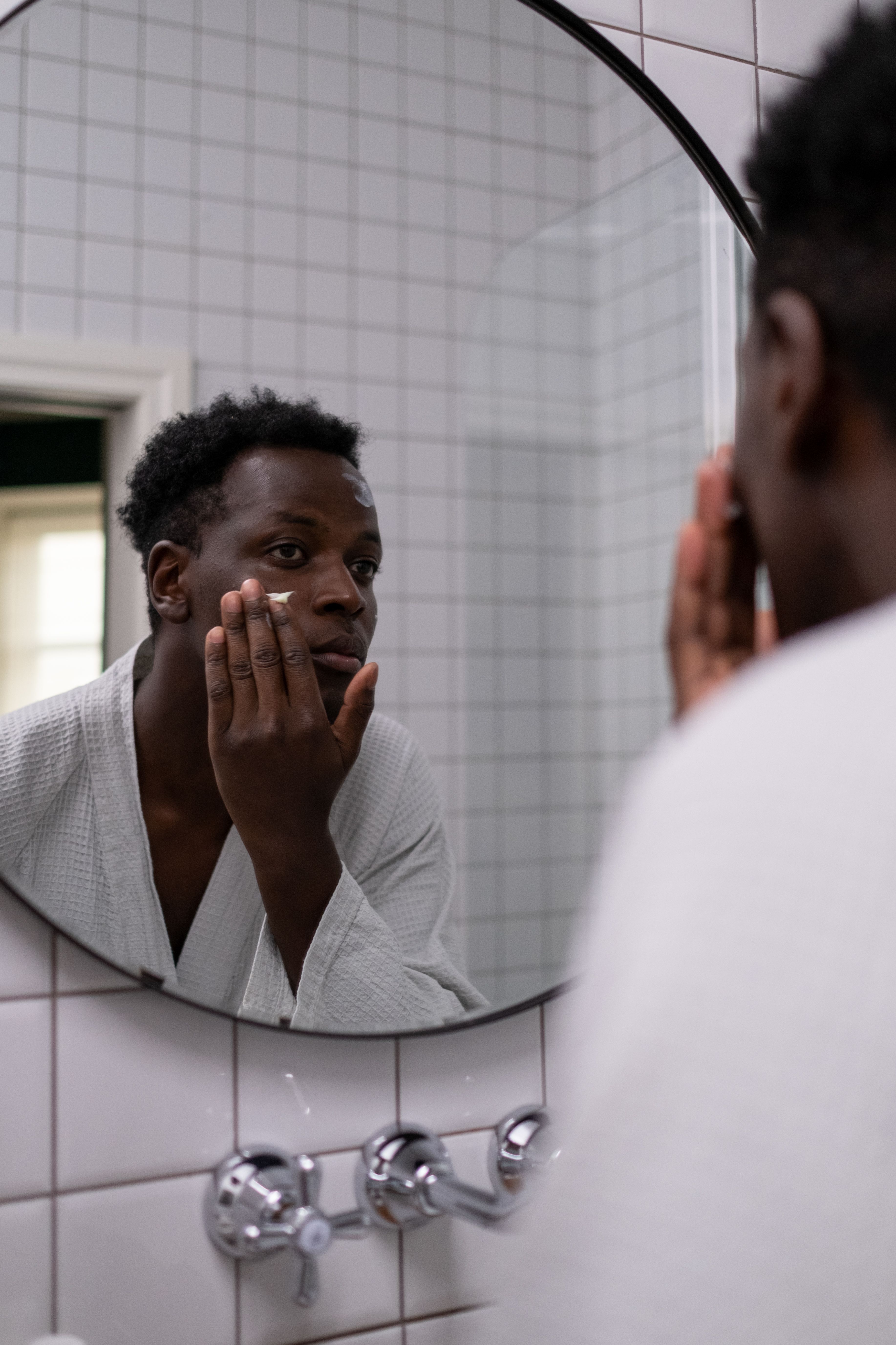 Man applying moisturizer to his face in a bathroom mirror