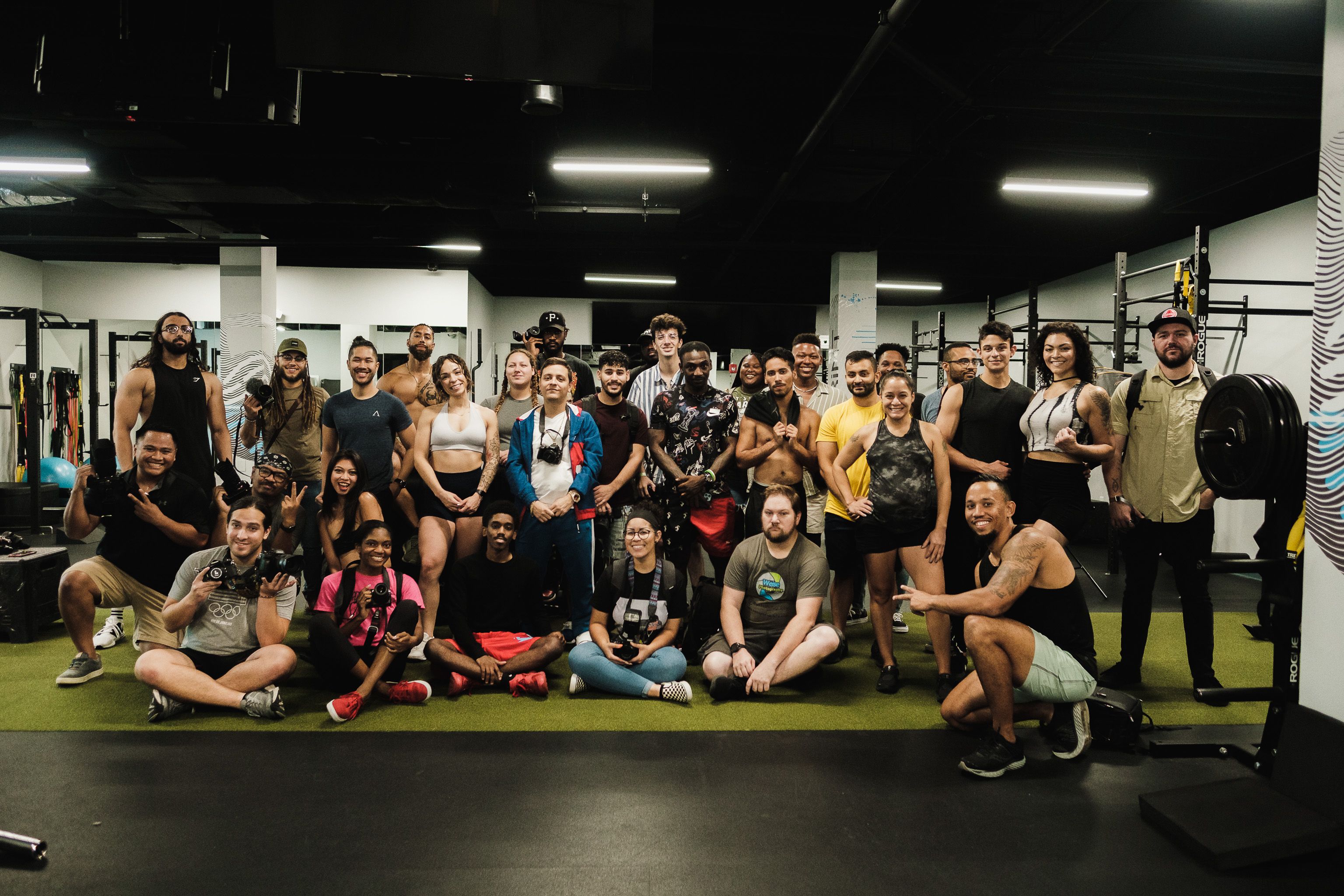 A diverse group of six members raising dumbbells overhead together during a group class