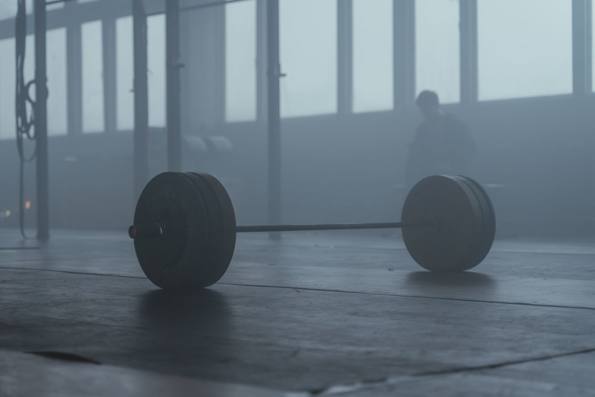 Loaded barbell resting on the floor in a moody, low-lit gym